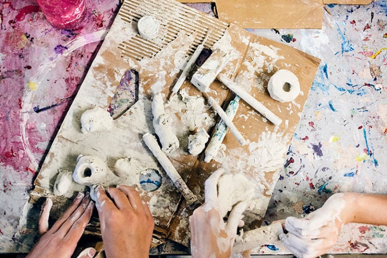 Hands shaping clay on a messy, colorful pottery workspace.