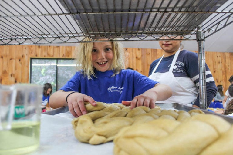 Child smiling while preparing challah bread in a kitchen setting.
