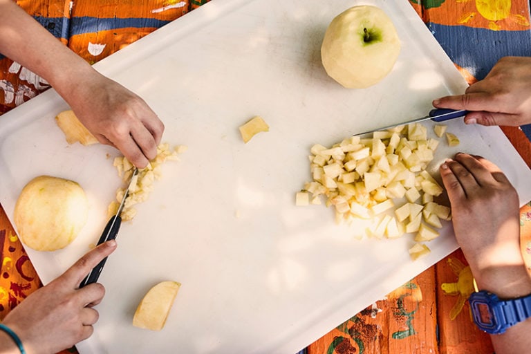 Two people slicing apples on a white cutting board.