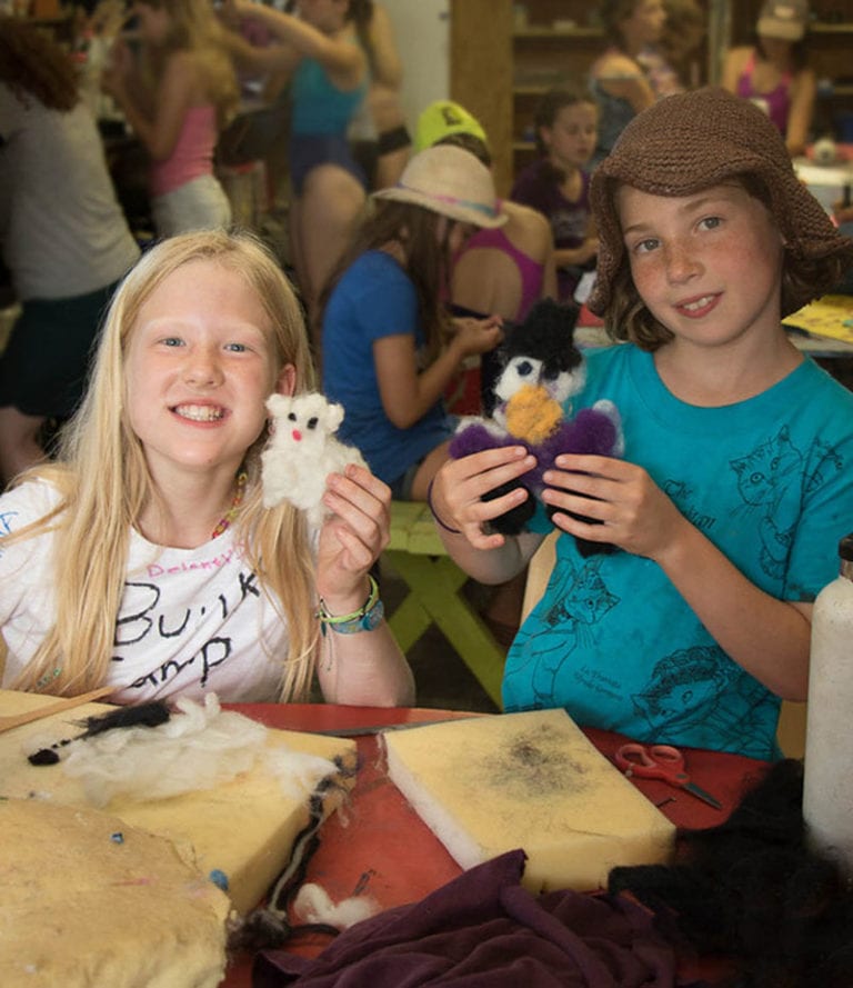 Two children in a classroom holding felted animal crafts.