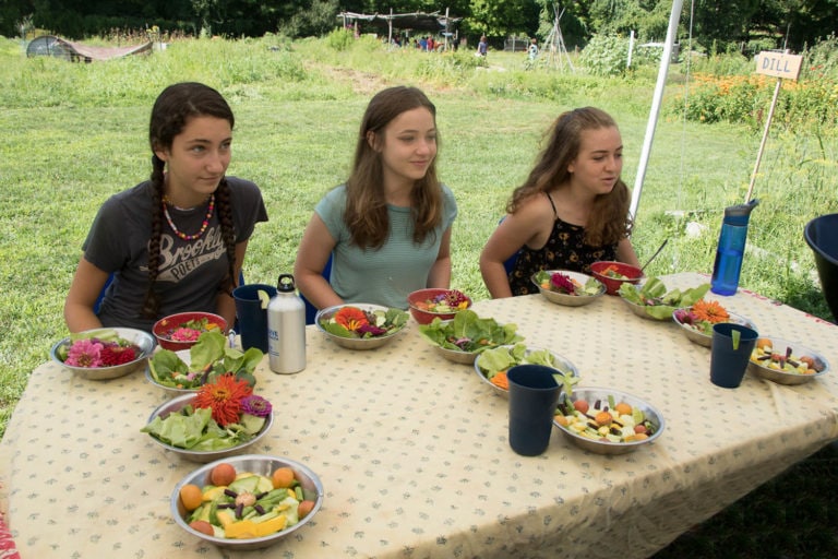 Three girls seated at an outdoor table with farm-to-table salads.