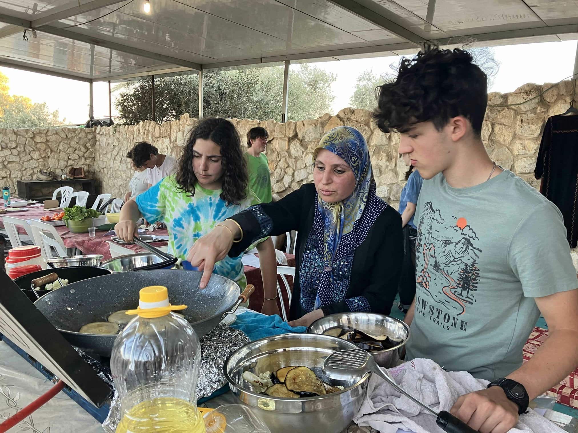 A woman and two individuals cooking together outdoors in a shared activity.
