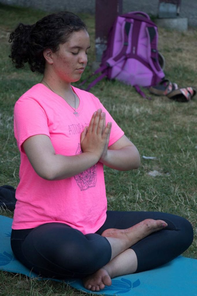 Person meditating outdoors on a yoga mat, wearing a pink shirt.