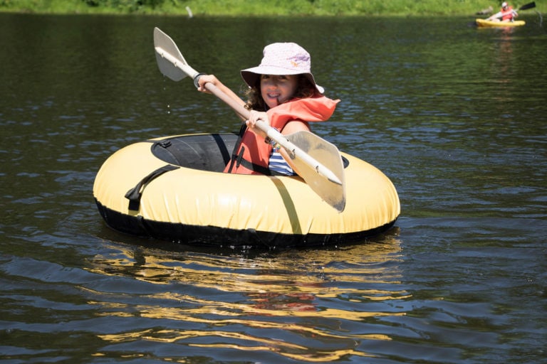 Child paddling an inflatable raft on a sunny day at the lake.