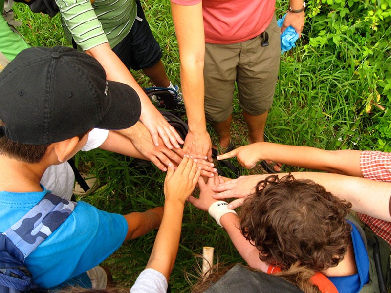 A group of children placing hands together in a circle outdoors.