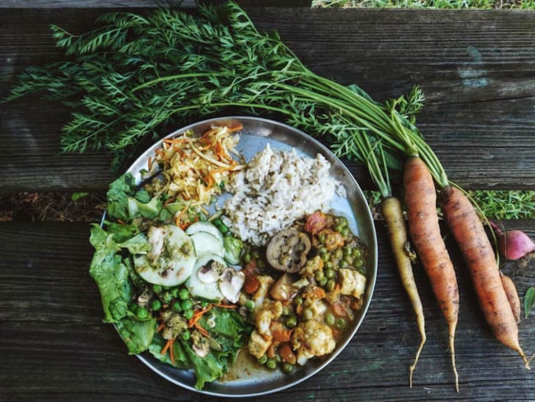 A dinner plate with salad and rice next to fresh farm carrots.