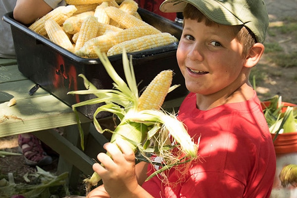 camper posing with husked corn