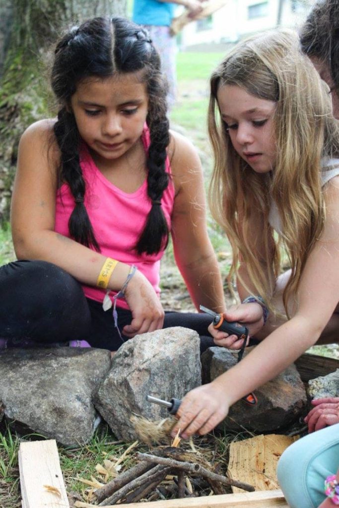 Two girls building a campfire with sticks and stones outdoors.